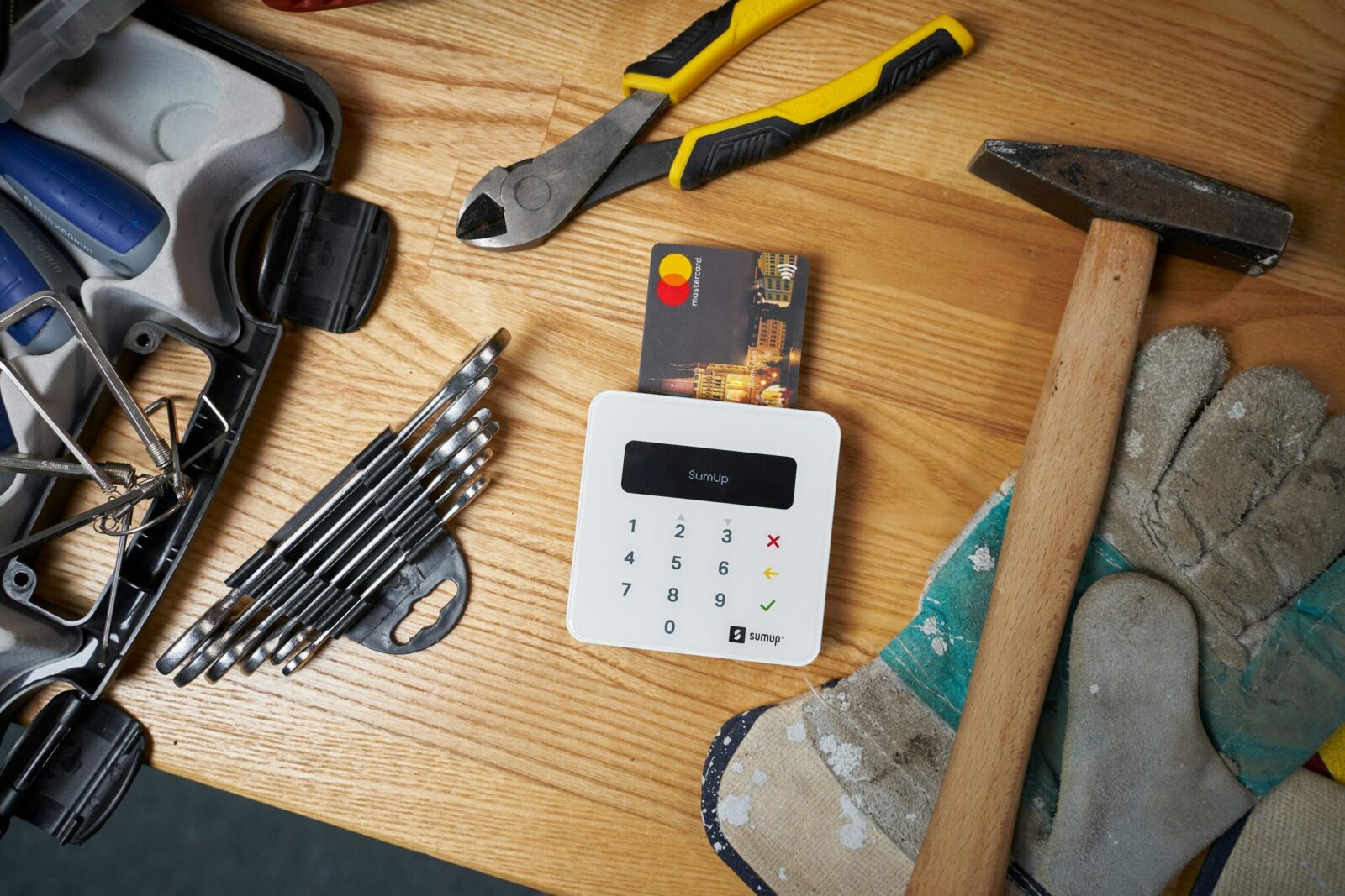 Overhead view of bright small plastic card in white contemporary wireless cash register surrounded by screwdriver set and hammer on big dirty gloves next to pliers