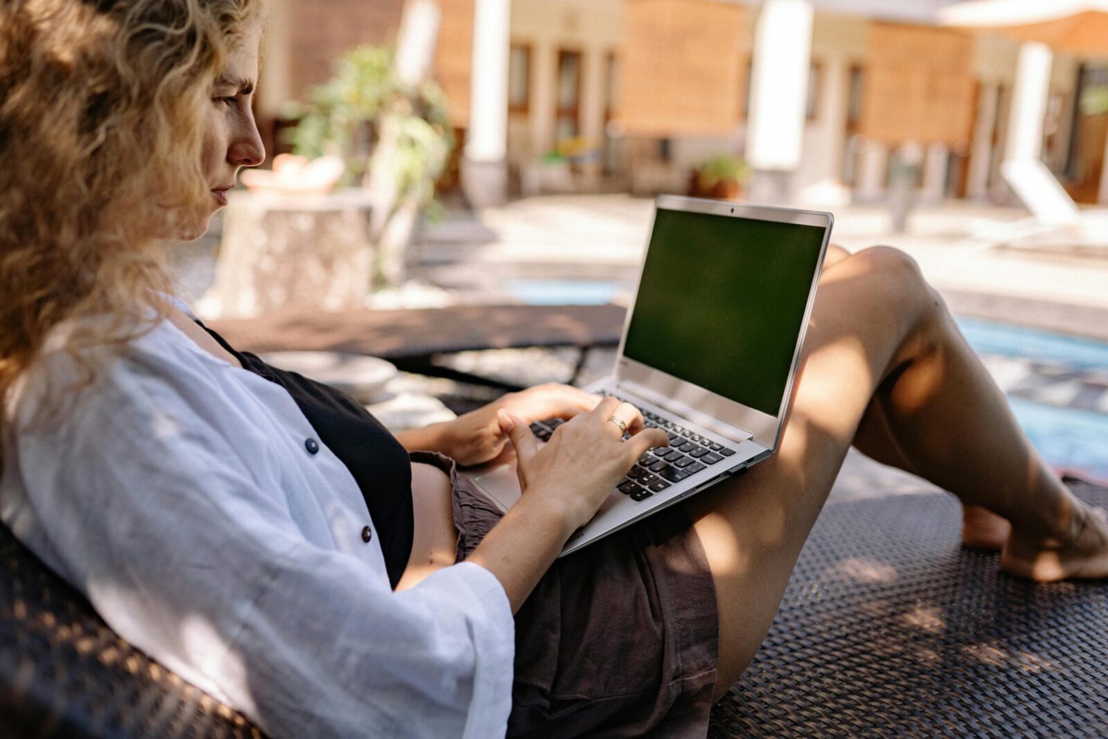 Relaxing professional woman working on a laptop outdoors by the poolside.