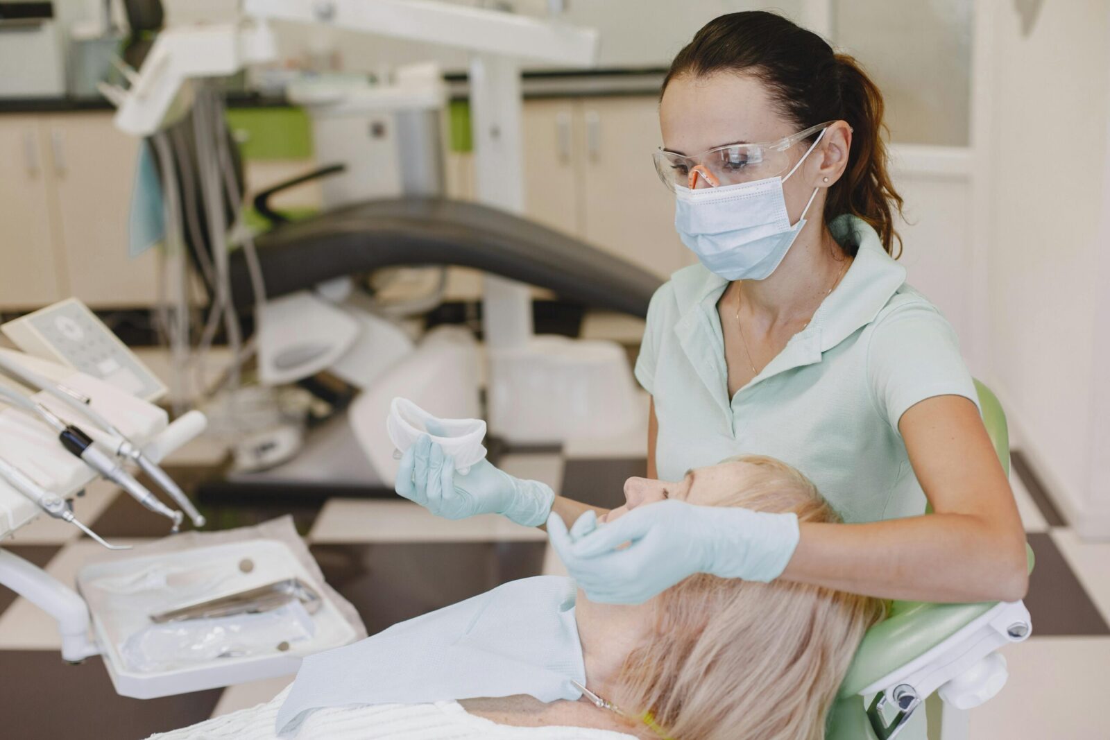 Female dentist with face mask examines patient in modern clinic. Healthcare setting.