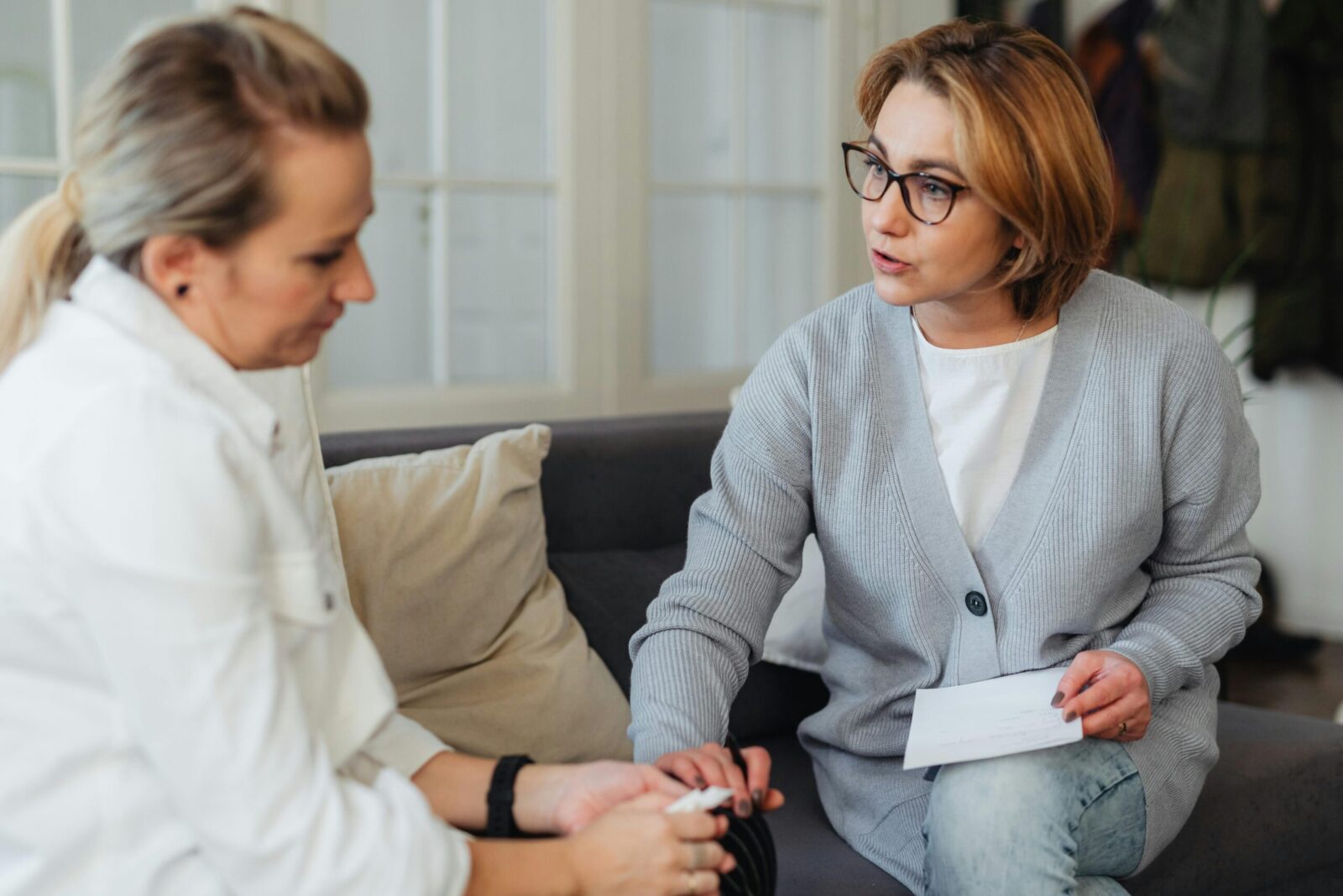Two adult women sitting indoors having a thoughtful conversation on a couch.