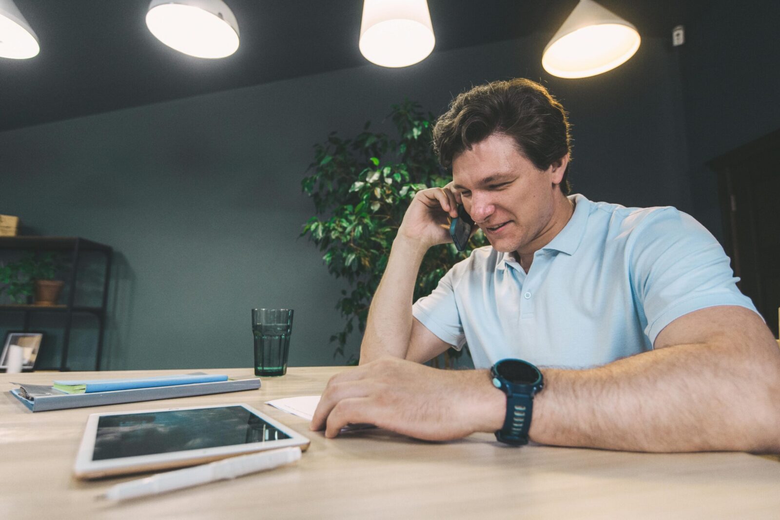 Businessman at a desk using a smartphone with a tablet, emphasizing digital connectivity.