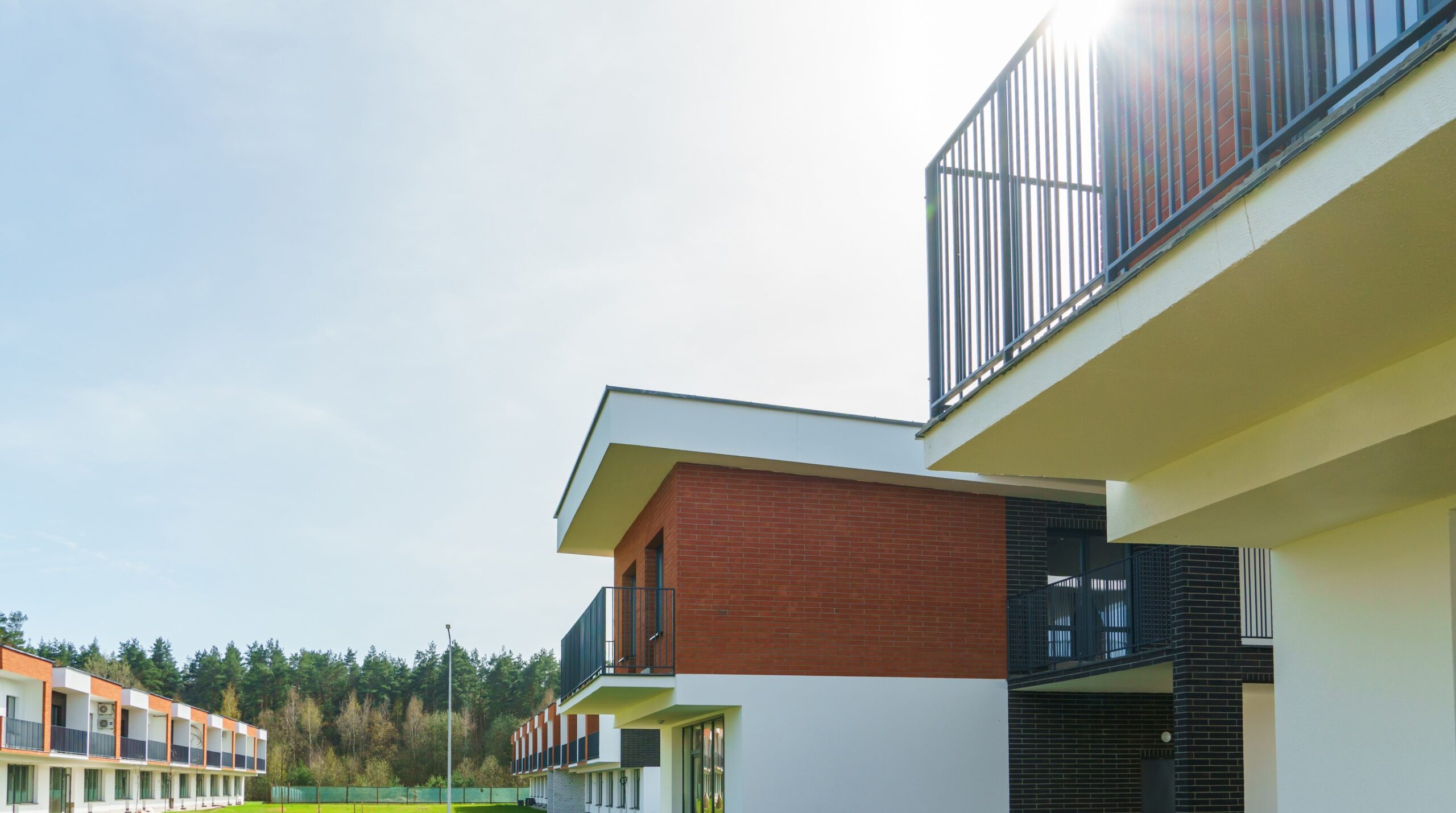 Photorealistic editorial still-life, 16:9. A modern suburban duplex viewed at a slight angle, split down the middle by a