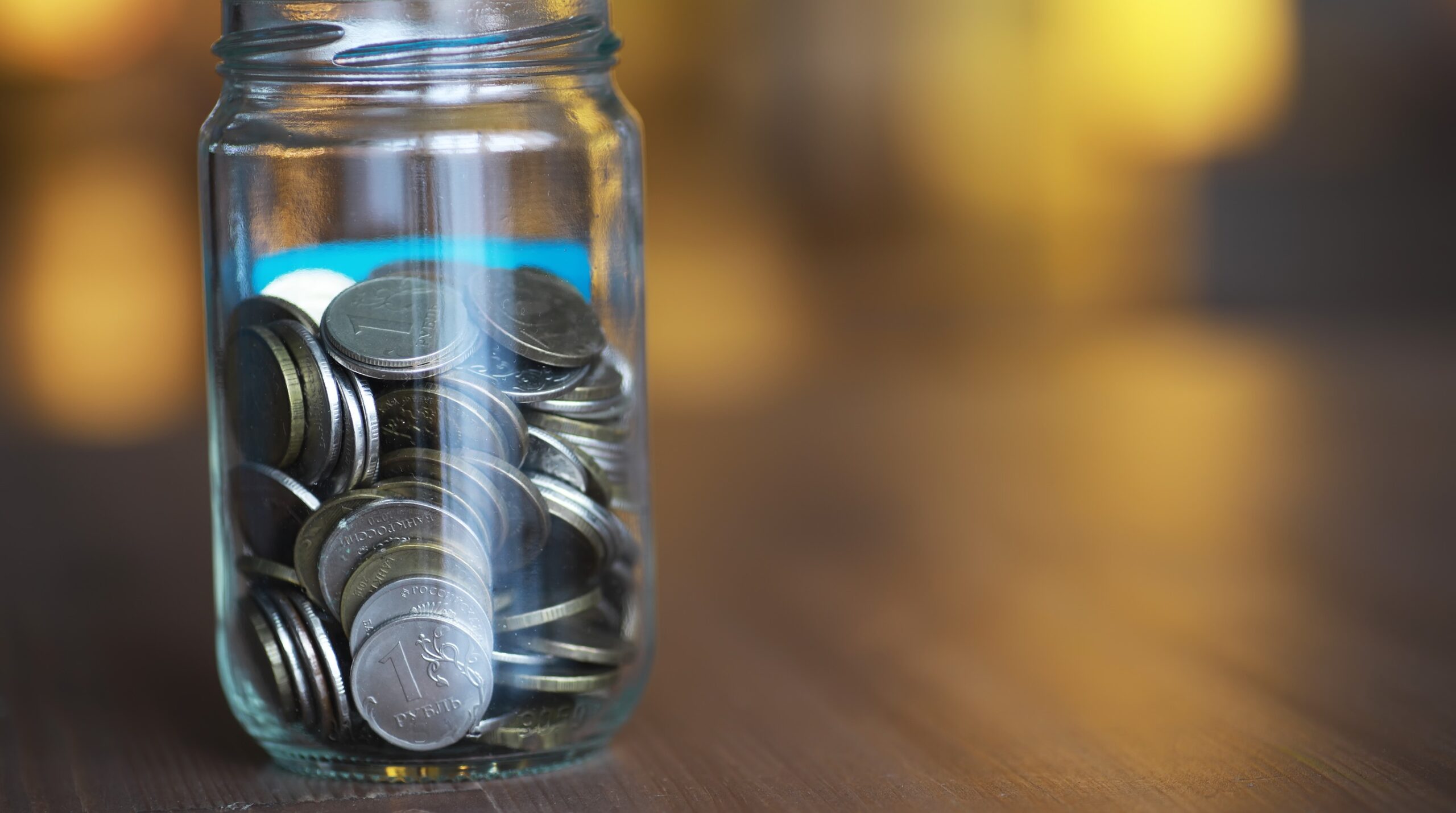 Photorealistic editorial still-life, 16:9. A glass jar of coins and folded cash sitting beside a stack of insurance poli